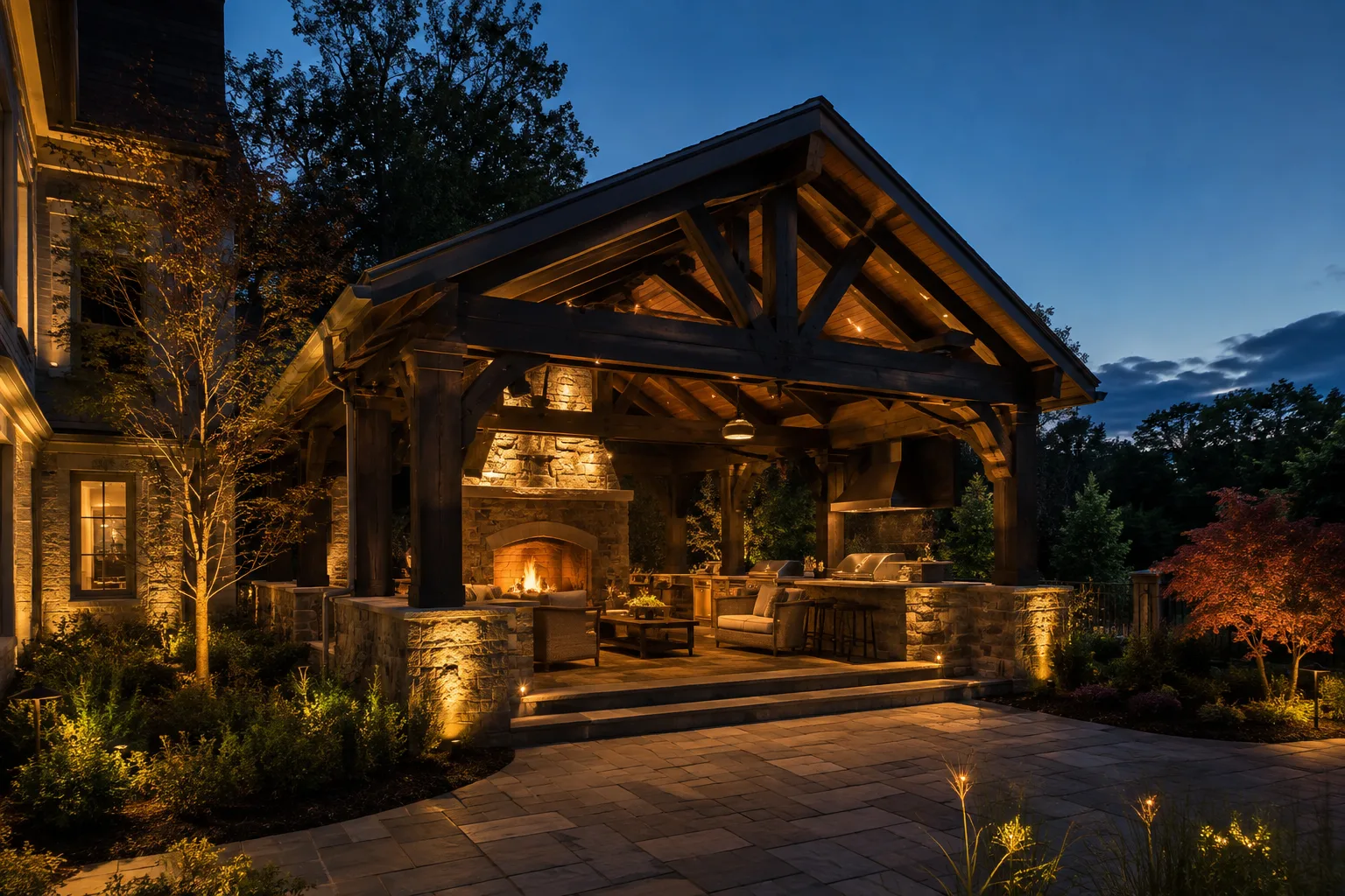 Covered outdoor living pavilion with stone fireplace and landscape lighting